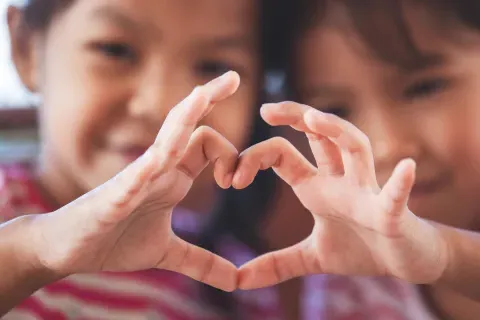 Two cute asian child girls making heart shape with hands together